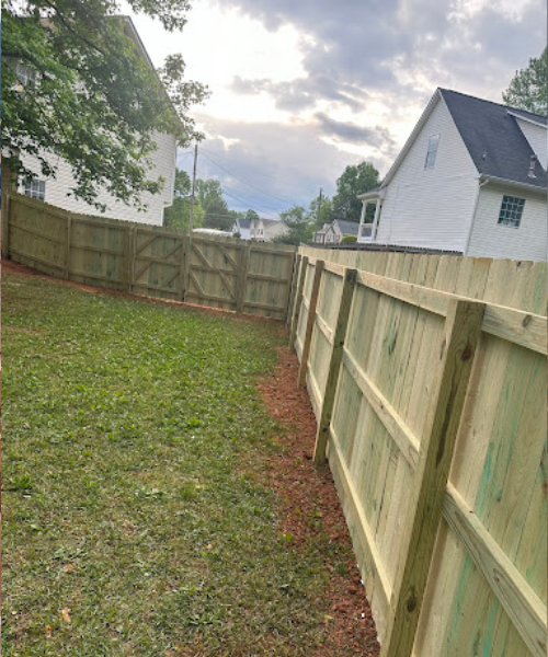 A backyard with a fence and a house in the background